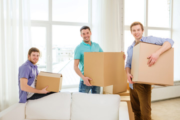 smiling male friends carrying boxes at new place