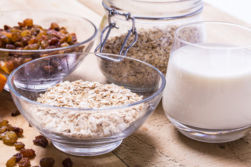 Bowl of oats, raisins cup of milk on the wooden table
