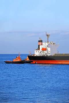 Tugboat assisting bulk cargo ship to harbor quayside