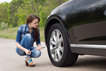 Young woman checking out a flat tyre on her car