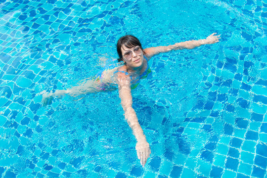 Beautiful young girl in sunglasses floating in the pool