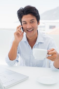 Smiling man having coffee and talking on phone