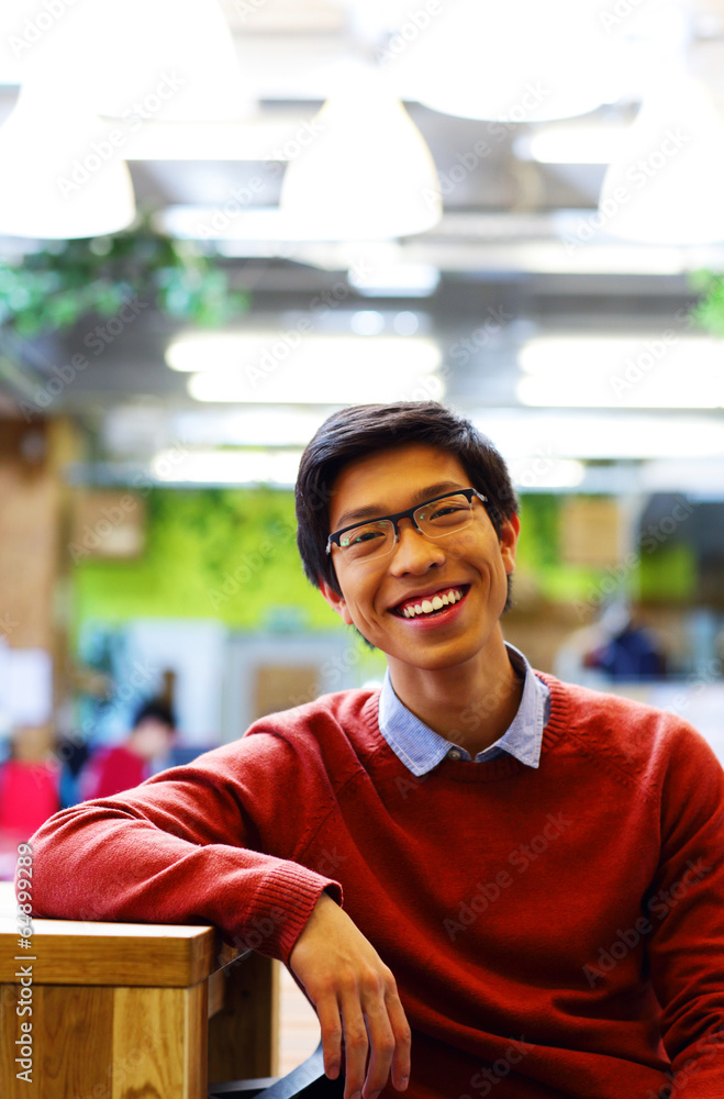 Poster Young cheerful asian student sitting at the table