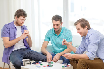 happy three male friends playing poker at home