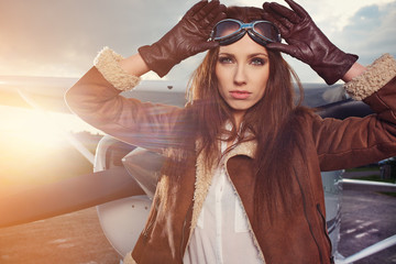 Portrait of young beautiful woman pilot in front of airplane.