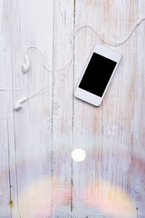 White smart phone with headphones on white wooden table surface