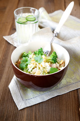Rice dish with broccoli, meat and eggs on old wooden table