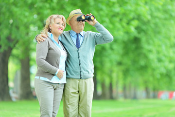 Senior couple looking through binoculars in park