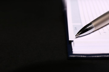 Pen on opened book on black table, close up