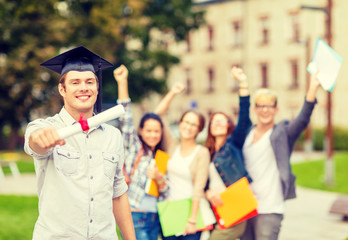 smiling teenage boy in corner-cap with diploma