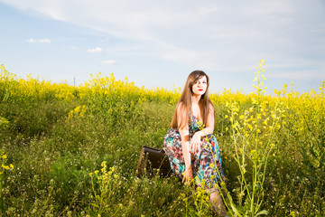 Naklejka na ściany i meble Girl with a suitcase in a field of yellow flowers