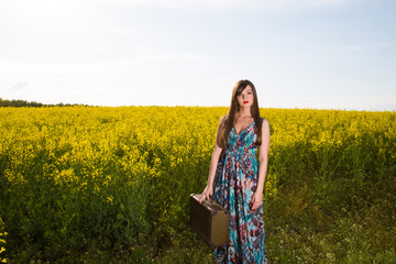 Girl with a suitcase in a field of yellow flowers