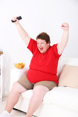 Fototapeta na wymiar Lazy overweight male sitting on couch and watching television