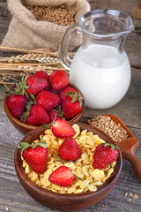 cornflakes in a wooden bowl with milk and strawberries