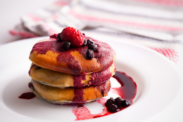 Stack of pancakes with berries on white plate