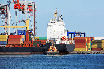 Fototapeta premium Tugboat assisting container cargo ship to harbor quayside