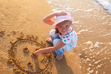 little girl draws sun on sand at the beach