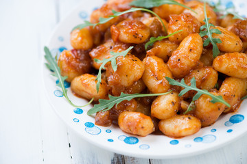 Boiled gnocchi with tomato sauce and arugula, close-up