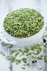 Glass bowl with split dried green peas over white wooden surface