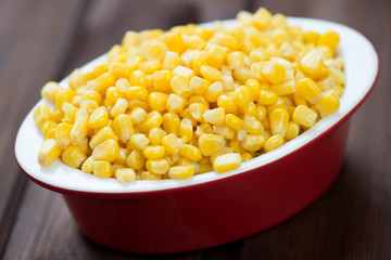 Glass bowl with corn kernels over wooden background, studio shot