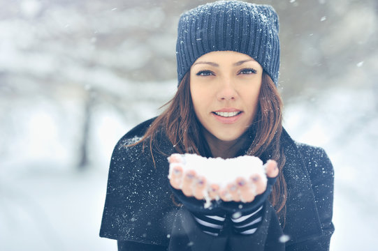 Young beautiful smiling girl holding snow in hands