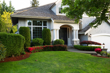 Clean exterior home with lush green grass yard, trees in bloom, and flowering bushes during spring time season 