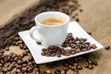 A cup of espresso and coffee beans on old wooden board