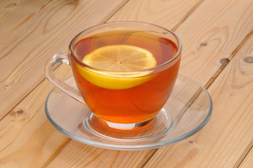 Glass cup with tea and a lemon on a glass saucer on a wooden tab