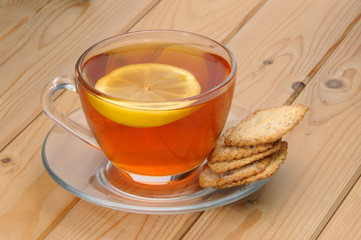 Glass cup with tea and a lemon on a glass saucer and cookies on