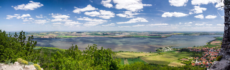 Fototapeta na wymiar Spring countryside with lake, village and blue sky with clouds