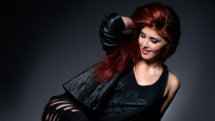 Beautiful redhead in black leather clothes isolated over gray