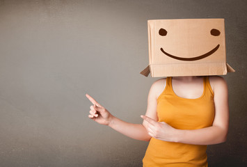 Young lady gesturing with a cardboard box on her head with smile - obrazy, fototapety, plakaty