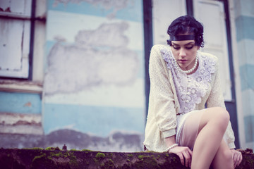 Brunette woman wearing pearls sitting in front of old  house