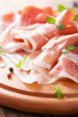 sliced prosciutto ham on chopping board with oregano and pepper