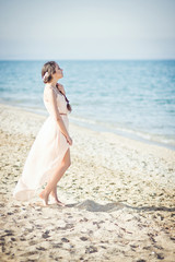 Fototapeta na wymiar Girl in a pink dress standing near the ocean