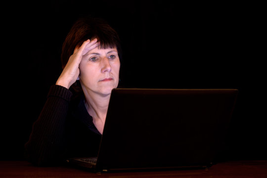 Mature Woman Working Late At Night, In Dark, Face Lit By Laptop