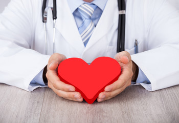 Midsection Of Doctor Holding Red Heart At Desk