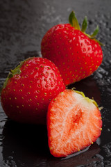 Three strawberries on black with water drops