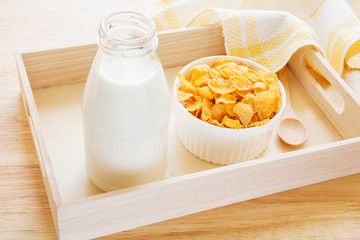 Bowl of cornflake and milk bottle on wooden tray