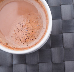 A mug of hot chocolate on a woven place mat.