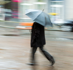 Man walking down the street on rainy day in motion blur