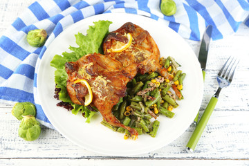 Roasted quails with vegetables on plate, on wooden background