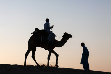 Single camel rider and person standing silhouetted dusk twilight