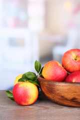 Ripe sweet apples with leaves in wooden bowl on light © Africa Studio