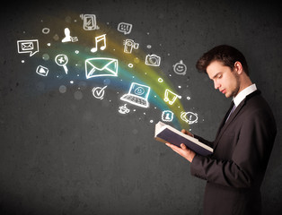 Young businessman reading a book with multimedia icons coming ou