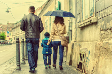Obraz na płótnie Canvas Mother, father and child walking together on a rainy day