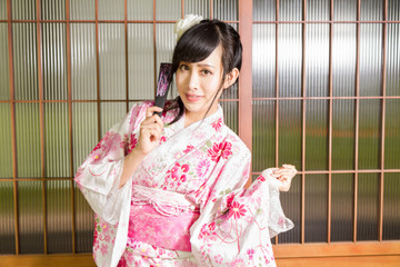 Asian woman wearing a kimono in front of Japanese wooden windows