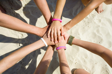 hands of young people stretching to the center on beach - Powered by Adobe
