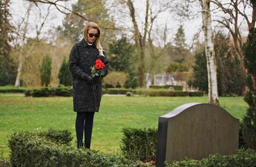 Naklejka na ściany i meble Sad woman grieves in a cemetery holding roses
