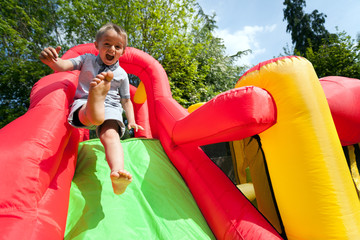 Child on inflatable bouncy castle slide - obrazy, fototapety, plakaty